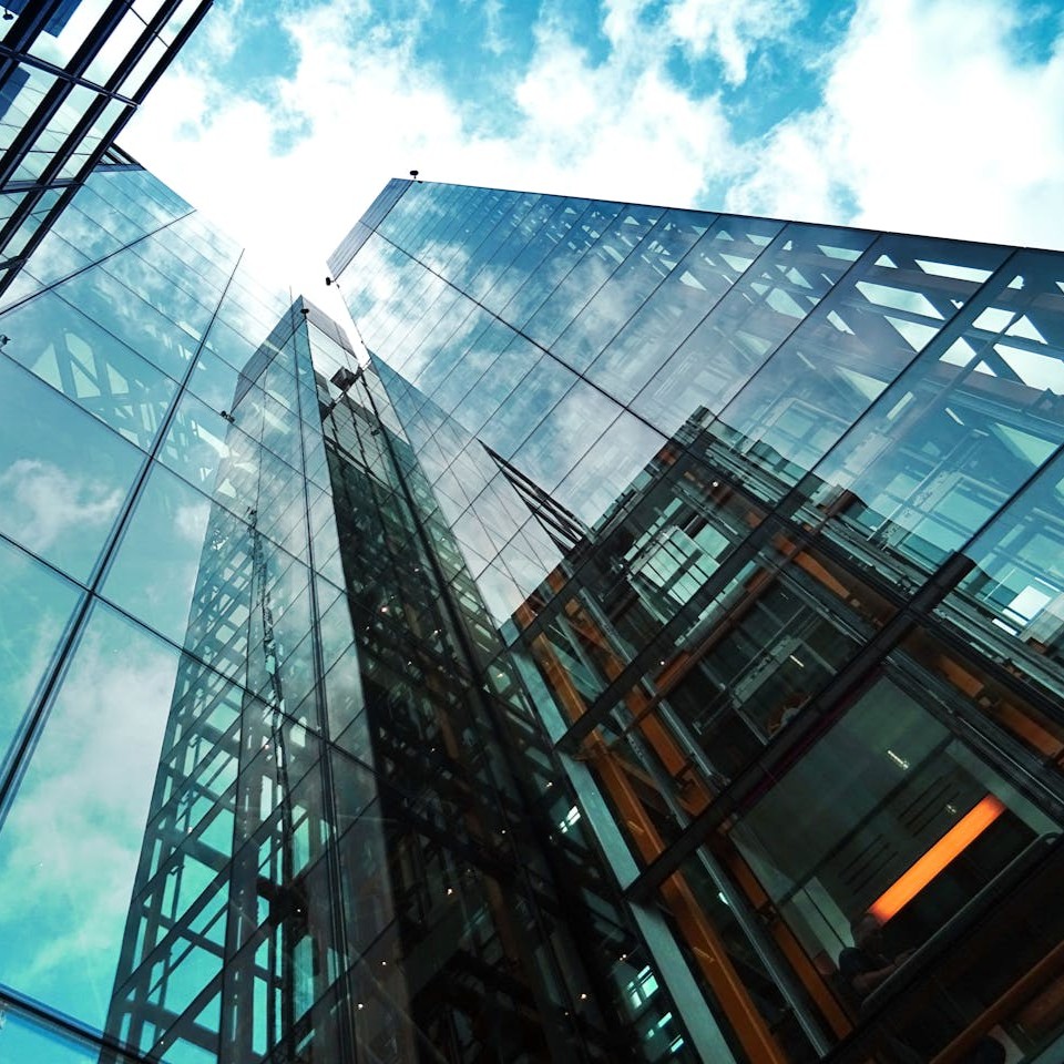 A View of a Tall Glass Building looking up at a Blue Sky with White Clouds